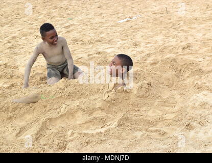 Jungen, die sich gegenseitig mit Sand am Strand Stockfoto