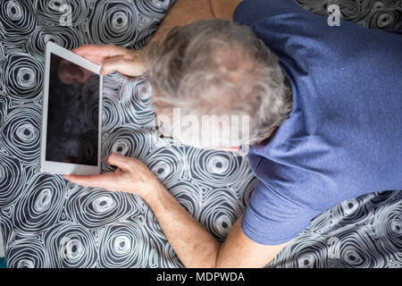 Antenne Portrait von älteren Mann liegend auf Bett mit Tablet Stockfoto