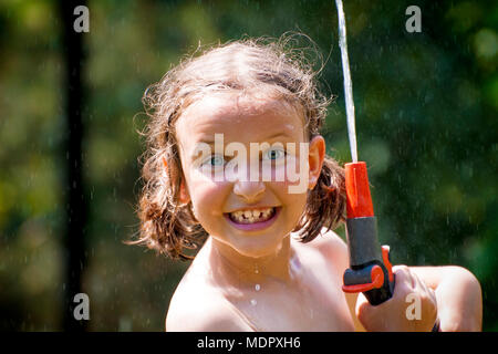 Junge Mädchen Spaß haben, während sie unter Garten Sprinkler im heißen Sommer Tag stehen. Stockfoto
