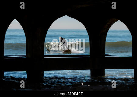 19.04.18. BOURNEMOUTH WETTER. Ein Paddel boarder surft eine Welle neben Bournemouth Pier als Temperaturen steigen an der Südküste von England. Stockfoto