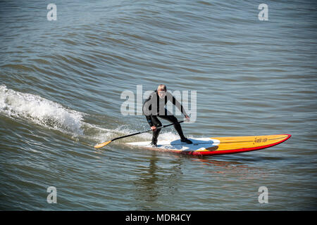 19.04.18. BOURNEMOUTH WETTER. Ein Paddel boarder surft eine Welle neben Bournemouth Pier als Temperaturen steigen an der Südküste von England. Stockfoto