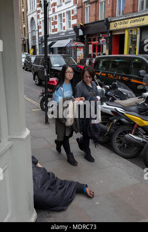 Passanten vorbei an einem Obdachlosen Mann, dessen Hand auf dem Bürgersteig ist in der großen Newport Street, am 16. April 2018 in London, England. Stockfoto