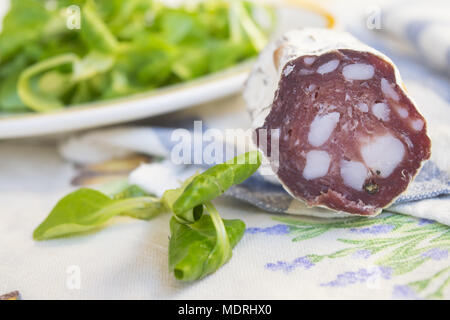 Stück Salami, geräucherte Wurst in der Nähe von einem frischen Salat Salat Stockfoto