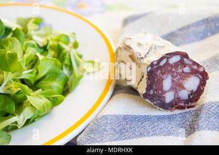 Stück Salami, geräucherte Wurst in der Nähe von einem frischen Salat Salat Stockfoto