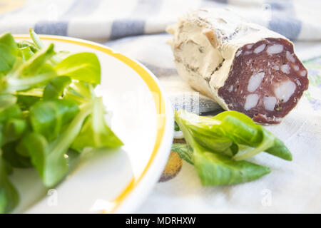 Stück Salami, geräucherte Wurst in der Nähe von einem frischen Salat Salat Stockfoto