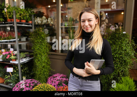 Weibliche hübsche Manager von Flower Shop stehend mit Tablet in der Nähe von Zimmerpflanzen. Stockfoto