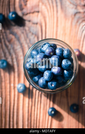 Frisch Blaubeeren in jar gestellt wurden. Einige Früchte frei auf alten hölzernen Tisch verstreut. Von oben geschossen Stockfoto