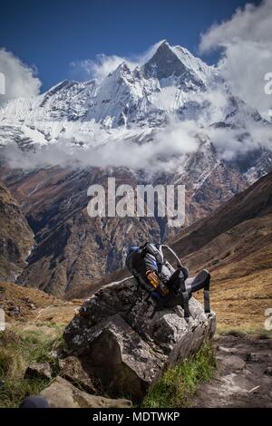 Ein Rucksack sitzt auf einem Felsen im Vordergrund. Im Hintergrund ist matschaputschare Fish-tail Berg, Teil des Annapurna Massivs in Nepal Stockfoto