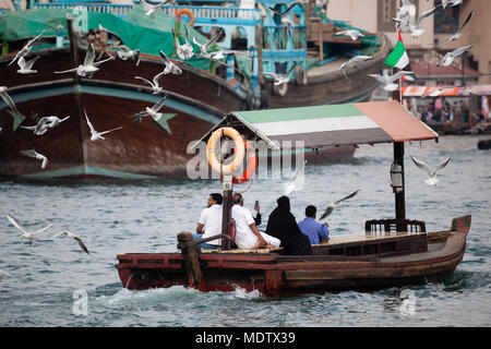 Die lokale Bevölkerung den Dubai Creek Kreuzung auf ein Abra mit dhaus im Hintergrund und Möwen hinter Fliegen, Dubai, Vereinigte Arabische Emirate, Naher Osten Stockfoto