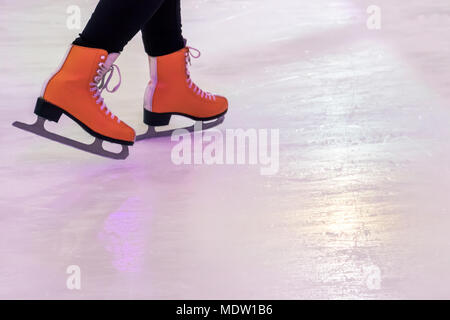 Nahaufnahme der weiblichen Füße in Schlittschuhen auf dem Eis. Der Orange Frauen Skates mit Reflexion auf weißem Eis. Stockfoto