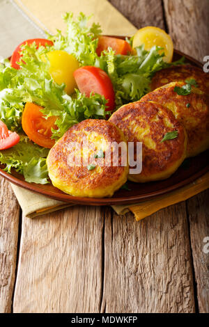 Ecuadorianischen traditionelles Essen: llapingachos Kartoffelpuffer und frischen Salat close-up auf einem Teller auf dem Tisch. Vertikale Stockfoto