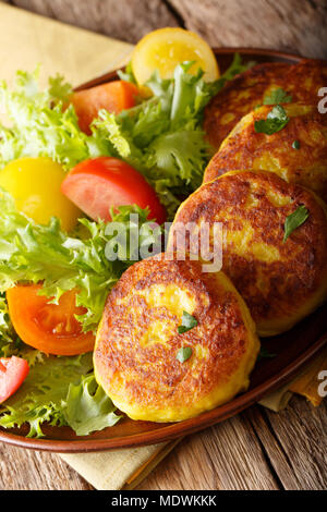Ecuadorianischen Kartoffelpuffer llapingachos und frischen Salat close-up auf einem Teller auf dem Tisch. Vertikale Stockfoto
