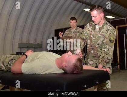 Staff Sgt. David Dillow, 386 Expeditionary medizinische Gruppe physikalische Therapie Techniker, Maßnahmen der rechten Schulter Bewegungsbereich des älteren Flieger Calvin Lourens, 386 Expeditionary Logistik Bereitschaft Squadron Passenger Service Specialist, Dez. 7, 2017, während Kapitän Eric Walter, 386 EMDG-physikalische Therapie element Chief, beobachtet an einem geheimen Ort im Südwesten Asien. (U.S. Air Force Foto von Tech. Sgt. Louis Vega Jr.) Stockfoto