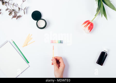 Frau prüfen Kosmetik pH-Wert durch die Verwendung von lackmuspapier und Skala. Blick von oben auf die weibliche Hand passende Reaktion Farbe auf weißem Hintergrund. Stockfoto