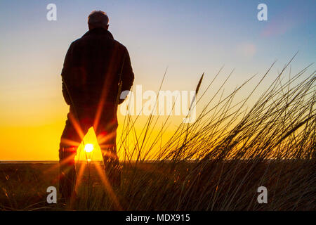 Atemberaubenden Sonnenuntergang, Southport, Merseyside. April 2018 20. UK Wetter. Ein Mann steht auf den Sanddünen beobachten wie der Sonnenuntergang in den Horizont über Southport Strand fällt in Merseyside. Credit: cernan Elias/Alamy leben Nachrichten Stockfoto
