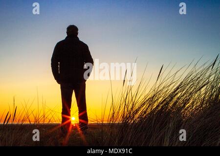 Atemberaubenden Sonnenuntergang, Southport, Merseyside. April 2018 20. UK Wetter. Ein Mann steht auf den Sanddünen beobachten wie der Sonnenuntergang in den Horizont über Southport Strand fällt in Merseyside. Credit: cernan Elias/Alamy leben Nachrichten Stockfoto