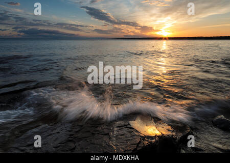 Sunrise leuchtet auf einem felsigen Lake Superior Shoreline als Welle stürzt über Sandstein. Dramatische Wolken Licht am frühen Morgen sky Stockfoto