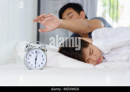 Verschlafene Mann, der versucht, schalten Sie Wecker neben eine Frau durch laute Wecker am Morgen gestört Stockfoto