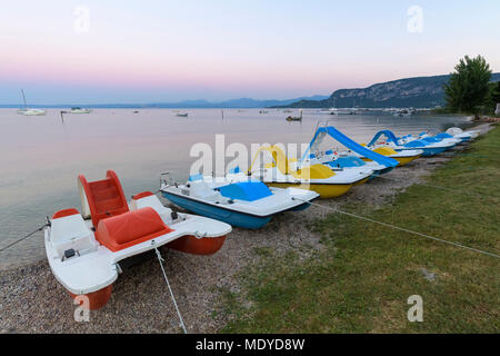 Reihe von farbenfrohen Tretboote am Strand bei Sonnenaufgang am Gardasee (Lago di Garda) in Bardolino in Venetien, Italien Stockfoto