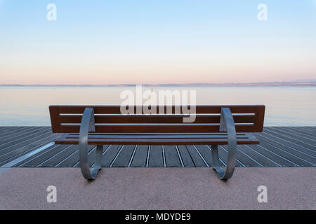 Promenade mit Parkbank bei Sonnenaufgang mit Blick auf den Gardasee (Lago di Garda) in Bardolino in Venetien, Italien Stockfoto