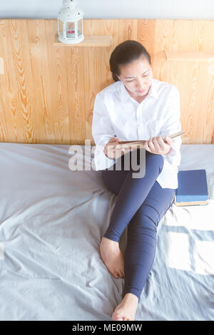 Soft Image der jungen Asain Frau mit Buch auf dem Bett im Schlafzimmer Stockfoto