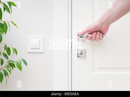 Männliche hand mit modernen Türgriff. Close-up-Elemente im Inneren der Wohnung. Weiße Tür und Schloss mit Schlüssel. Der Lichtschalter an der Wand ein Stockfoto