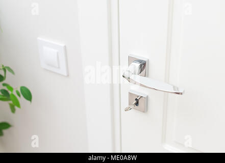 Stilvolle metall Türgriff und Rosette für Schloss mit Schlüssel. Close-up Elemente der Innenausstattung. Weiße Tür und weiße Wand mit Schalter Stockfoto