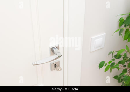 Modernes Metall Türgriff und Rosette für Schloss mit Schlüssel. Close-up Elemente der Innenausstattung. Weiße Tür und weiße Wand mit Schalter Stockfoto