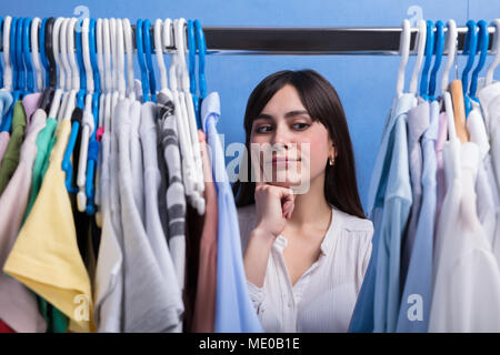 Junge Frau auf der Suche nach Kleidung auf Kleiderstange In Store Stockfoto