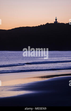 Silhouette von Cape Byron Lighthouse auf einem Hügel und am Strand bei Sonnenuntergang bei Byron Bay in New South Wales, Australien Stockfoto