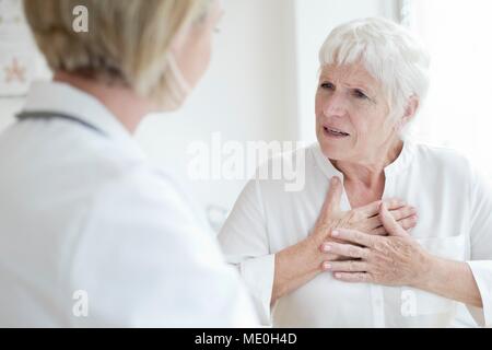 Ältere Frau Brust berühren und im Gespräch mit Frau Doktor. Stockfoto