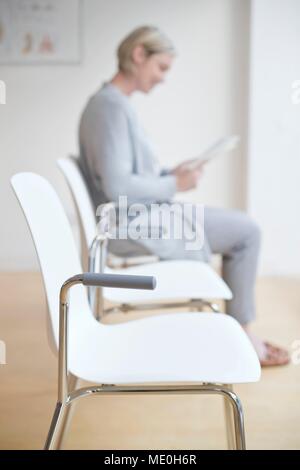Frau sitzt in der Arzt, der Warteraum lesen Magazin. Stockfoto