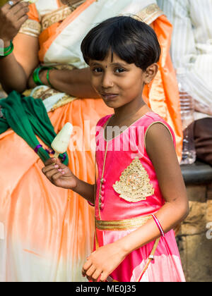 Ein junges Mädchen in einem hellen Rosa Kleid essen ein Popsicle und Lächeln für die Kamera; Mumbai, Maharashtra, Indien Stockfoto