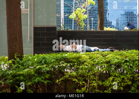 18.04.2018, Singapur, Republik Singapur, Asien - ein Mann schläft hinter einer Hecke in Singapore's Central Business District in der Innenstadt. Stockfoto