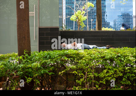 18.04.2018, Singapur, Republik Singapur, Asien - ein Mann schläft hinter einer Hecke in Singapore's Central Business District in der Innenstadt. Stockfoto