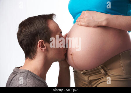 Junger Mann küssen Bauch der schwangeren Frau auf weißem Hintergrund Stockfoto