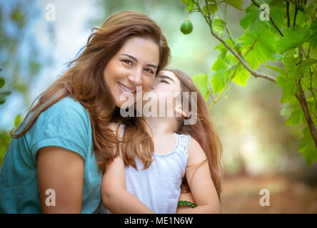 Porträt eines niedlichen kleinen Mädchen küsste ihre Mutter, glückliche Familie mit Freude die Zeit zusammen in die Früchte Garten, genießen Frühling Natur und Stockfoto