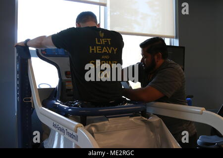 Jose Perez, eine physikalische Therapie Assistent an den unerschrockenen Geist in Fort Bragg, N.C., hilft ein Patient in den Alter-G Anti-Gravity Laufband, Dez. 18, 2017. Die zip-in-Laufband mit Luft füllt, und Maßnahmen, die das Körpergewicht des Patienten. Perez, stellen Sie die Maschine einen bestimmten Prozentsatz des Gewichts des Patienten zu entfernen, so dass er langsam zurück in Laufen und Gehen Intervalle mit weniger Widerstand zu erleichtern. (U.S. Armee Foto von Sgt. Paige Behringer) Stockfoto