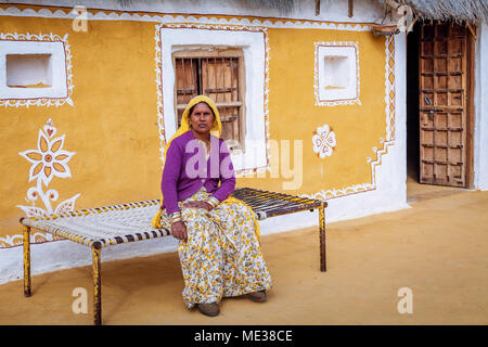 Rajasthani im Alter von Tribal Frau vor einer Lehmhütte in einem Dorf in der Nähe der Wüste Thar Jaisalmer, Indien sitzen. Stockfoto