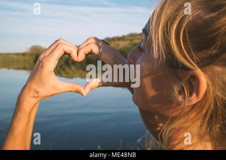 Junge Frau von der Seepromenade, die Form eines Herzens finger Rahmen auf schöne Landschaft, Reflexion über die Wasseroberfläche. Die Menschen reisen Liebe Umwelt Stockfoto