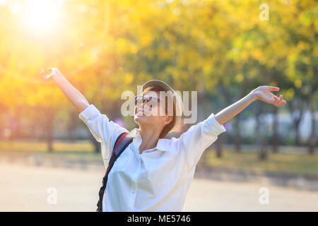 Junge asiatische Frau mit weißem Hemd und Sonnenbrille steigende Hand mit Freiheit Gefühl in öffentliche Park Stockfoto
