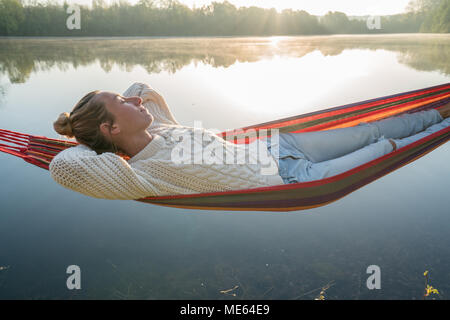 Junge Frau entspannen auf der Hängematte am See, Sonnenlicht, Sunbeam und Reflexion. Menschen Entspannung Wohlbefinden in der Natur. Frankreich, Europa Stockfoto