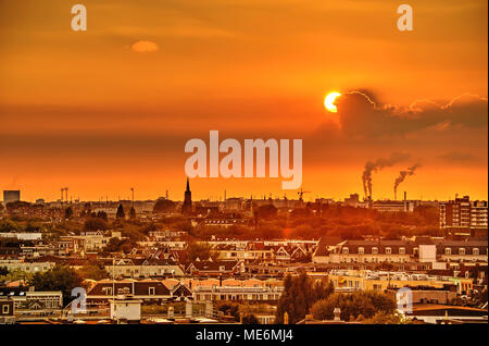 Die untergehende Sonne, teilweise verdeckt von Wolken, über einen Teil der westlichen Skyline, einschließlich Sparta Fußballstadion, ein Kirchturm und Schornsteine in der Stockfoto