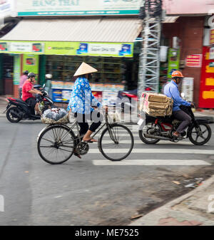 Eine weibliche Radfahrer tragen eine kegelförmige Hut reiten ihr Fahrrad neben Motorrädern in Ho Chi Minh City, Vietnam. Stockfoto