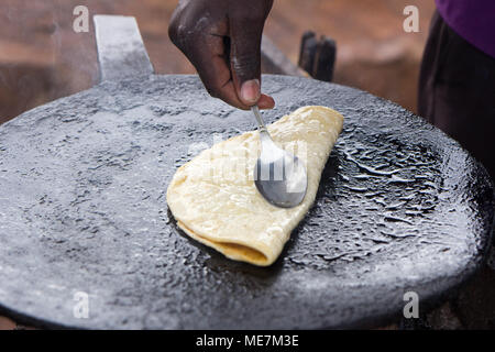 Ein fladenbrot "chapati" gebraten und mit einem Löffel durch eine native Ugandischen cook gefaltet. In Uganda im Mai 2017 erschossen. Stockfoto