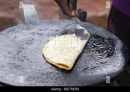 Ein fladenbrot "chapati" gebraten und mit einem Löffel durch eine native Ugandischen cook gefaltet. In Uganda im Mai 2017 erschossen. Stockfoto