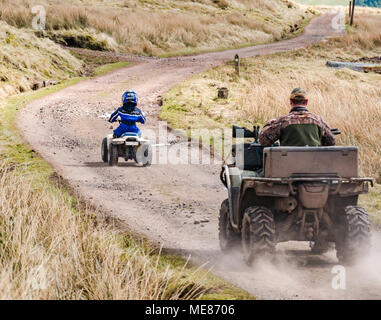 West Linton, Scottish Borders, Schottland, Vereinigtes Königreich, 21. April 2018. UK Wetter: Warme Frühlingssonne in der Landschaft, mit einem Jungen tragen ein Motorrad Helm fahren ein kleines quad bike auf einen Feldweg, von seinem Bauer Vater auf einem All Terrain Vehicle mit einer Schrotflinte auf der Motorhaube gefolgt Stockfoto