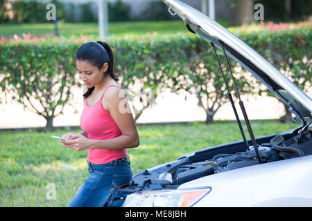 Closeup Porträt, junge Frau in Rosa tanktop Probleme mit ihrem kaputten Auto, Motorhaube zum Öffnen und texting für Hilfe zum Handy, grünen Bäumen isoliert Stockfoto