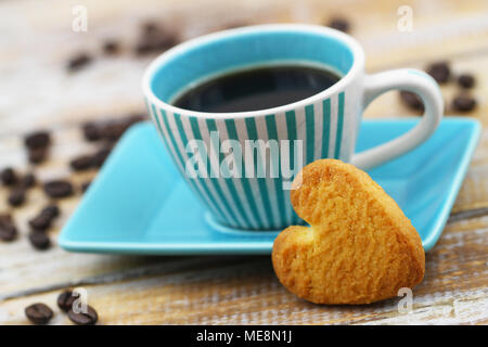 Herzförmige crunchy Cookie lehnte sich gegen die Tasse Kaffee auf Holzmöbeln im Landhausstil Oberfläche Stockfoto