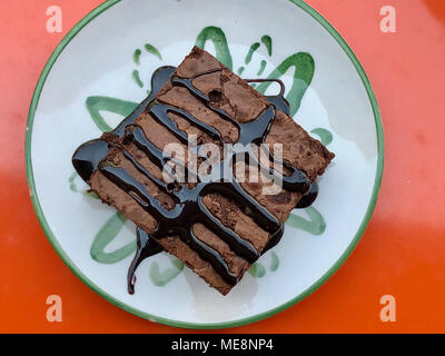 Brownie mit Schokoladensauce serviert im Cafe Shop auf Orange Oberfläche. Kalorienreiche Lebensmittel. Stockfoto